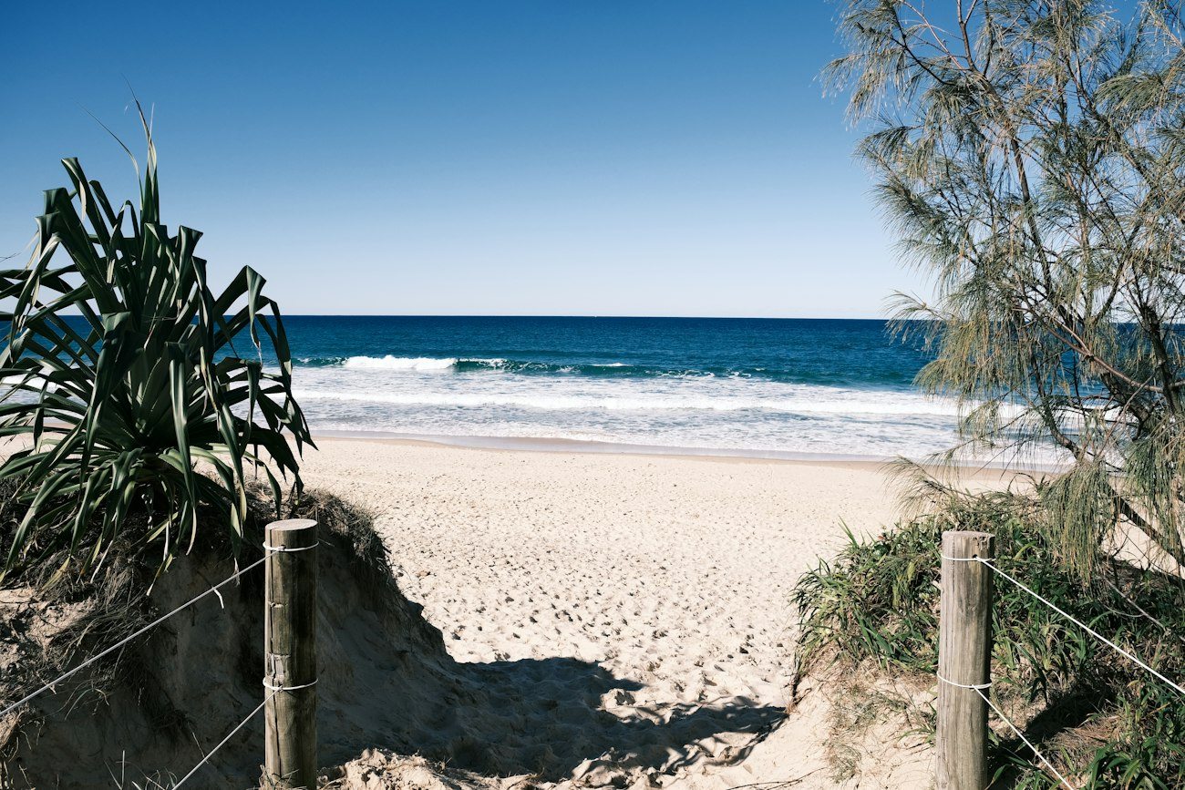 A sandy Sunshine Coast beach beyond a coastal path