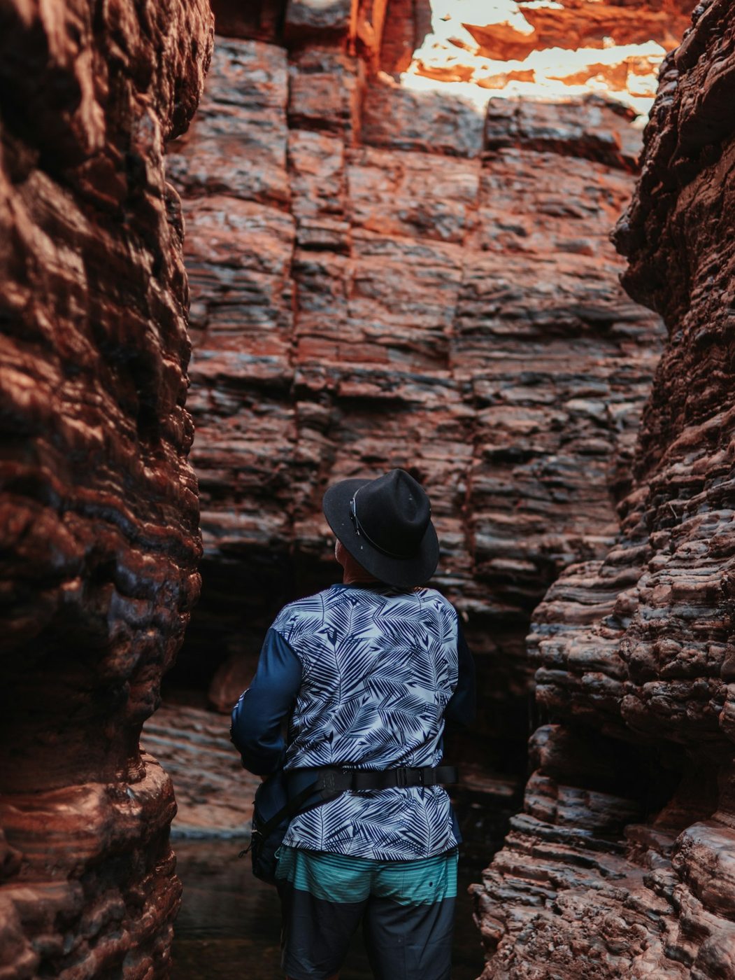 A visitor standing among layered red rocks in Karijini