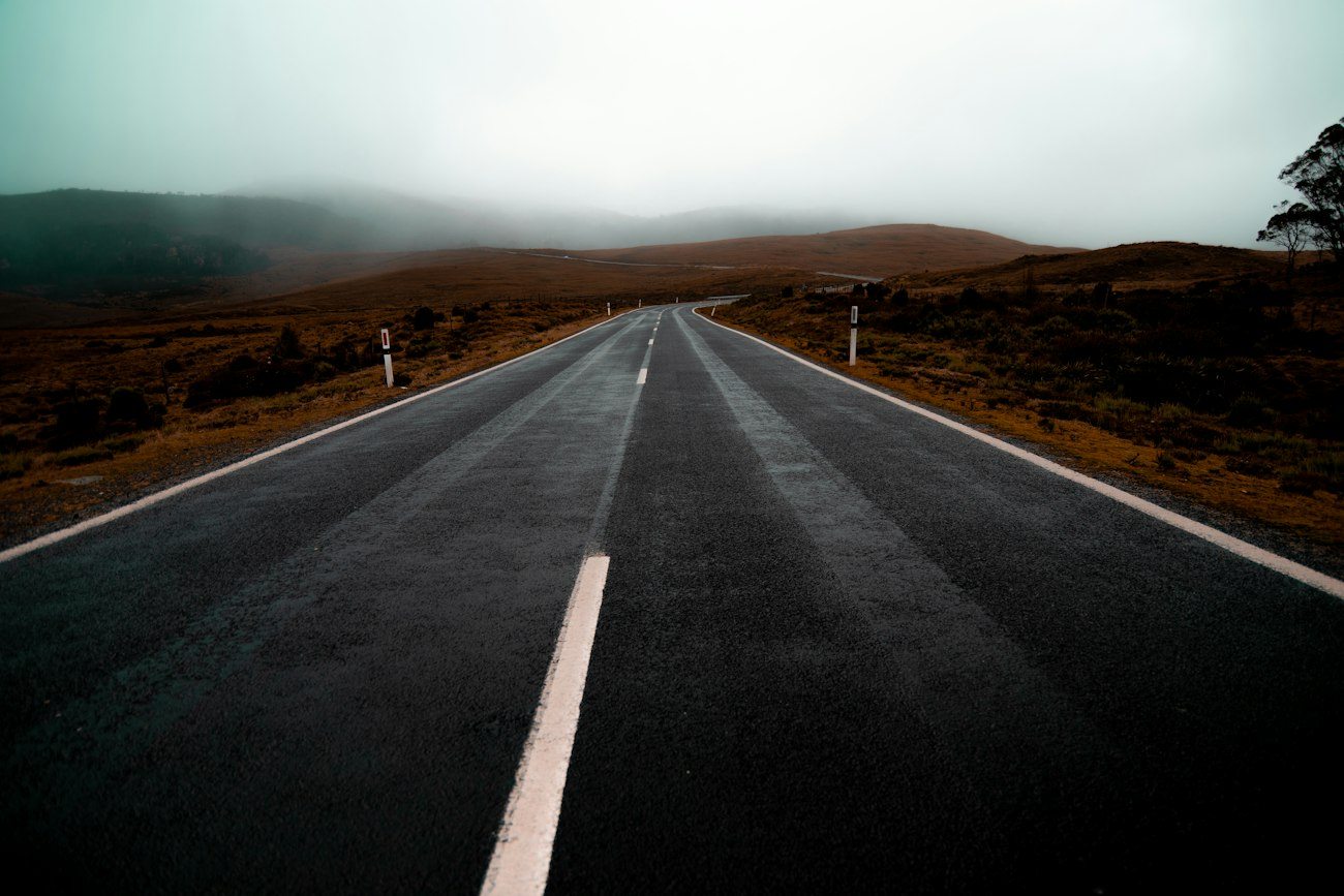 An empty road disappearing toward misty Tasmanian hills