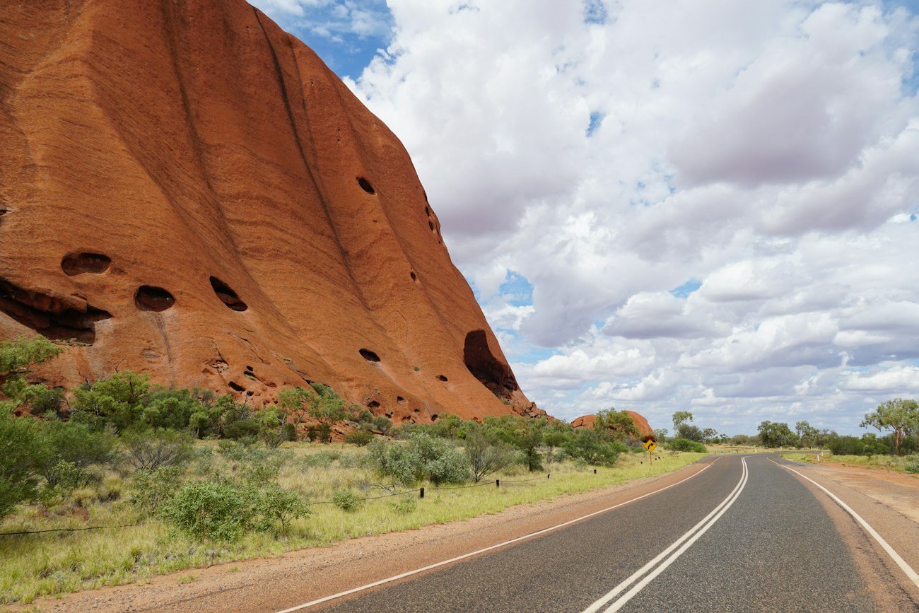 A paved road beside the red rock face of Uluru
