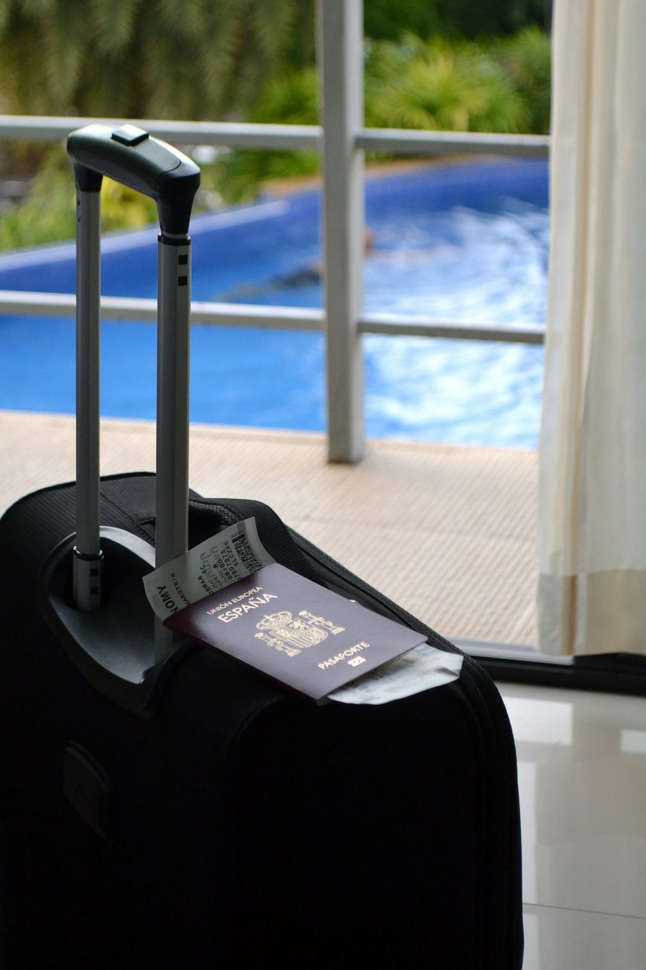 A passport resting on a suitcase beside a window